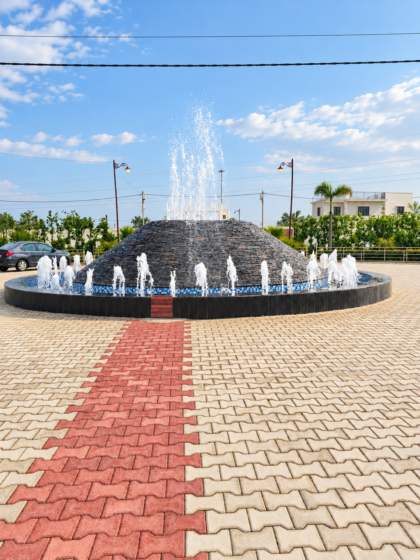 Portrait view of the working circular fountain with a central water jet and paved approach.